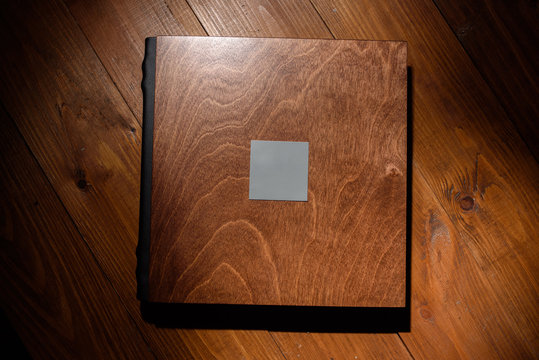 Photo book in a wooden cover on a wooden table. Hard light