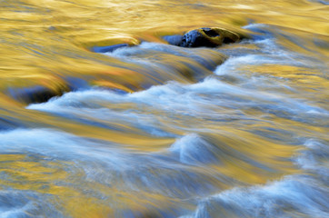 Autumn landscape of the Little River captured with motion blur and illuminated by reflected color from sunlit foliage and blue sky overhead, Great Smoky Mountains National Park, Tennessee, USA