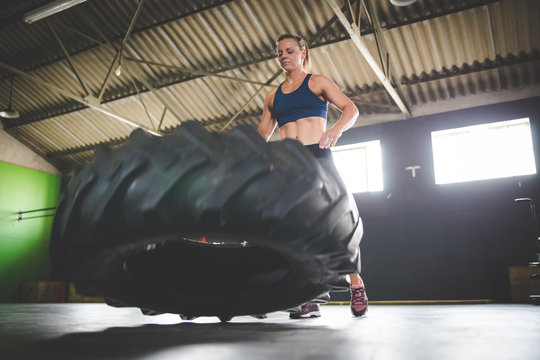 Female fitness model doing cross fit exercise with a massive tyre in a gym