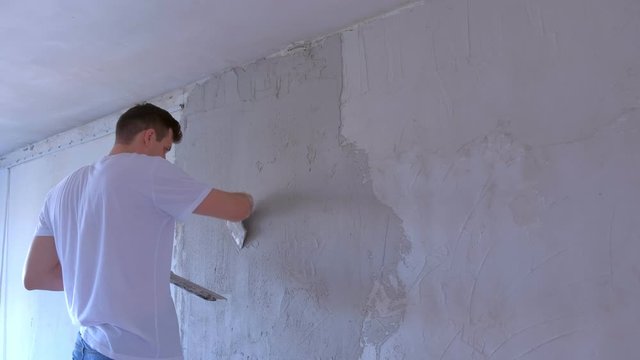 Plasterer man is applying plaster on wall to aligning wall using spatula. Finishing construction renovation works in apartment. Worker builder making overhaul applying putty on wall with trowel.