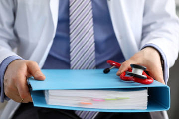 GP sitting in office holding in hands big binder