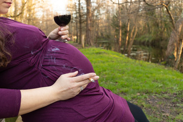 Pregnant woman drinking alcohol and smoking cigarette in park