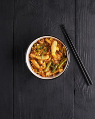 traditional dish of Asian cuisine is a WOK rice in a clay plate on a black wooden table.
