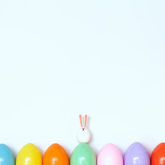 Top view of an Easter composition of painted eggs in bright juicy colors on a white background with a little rabbit. Holiday concept, flat layout, minimalism.