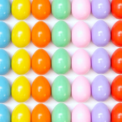 Top view of an Easter composition of painted eggs in bright juicy colors on a white background with a glossy texture that lie in even rows. Holiday concept, flat layout, background, advertisement.