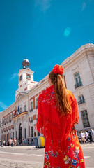 Fototapeta premium A young caucasian woman chulapa with red flower, traditional dress, and Spanish scarf at Puerta del Sol during San Isidro, the spring festival in May in the downtown of Madrid, the capital of Spain