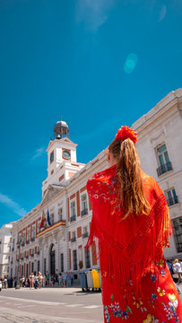 A young caucasian woman chulapa with red flower, traditional dress, and Spanish scarf at Puerta del Sol during San Isidro, the spring festival in May in the downtown of Madrid, the capital of Spain