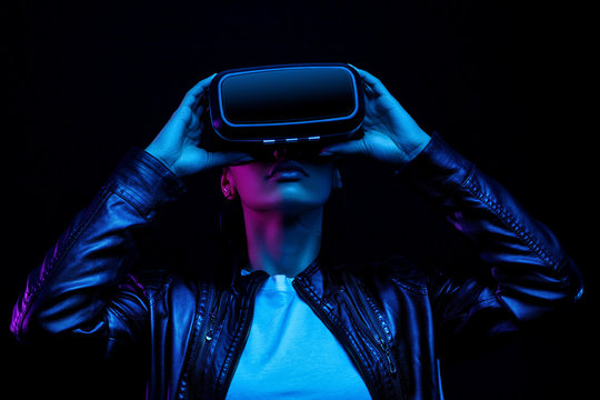 African american girl in vr glasses, watching 360 degree video with virtual reality headset isolated on black background, illuminated by neon lights