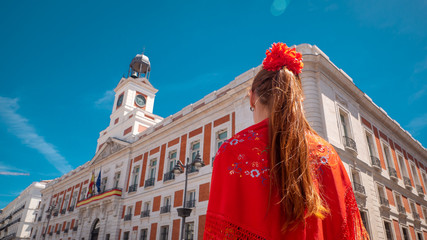 A young caucasian woman chulapa with red flower, traditional dress, and Spanish scarf at Puerta del...