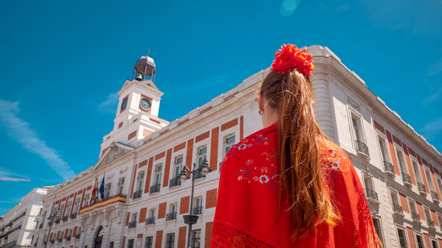 A young caucasian woman chulapa with red flower, traditional dress, and Spanish scarf at Puerta del Sol during San Isidro, the spring festival in May in the downtown of Madrid, the capital of Spain