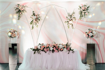 The festive table for the newlyweds is decorated with many blooming pastel-pink and white flowers and greenery