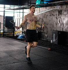 Fototapeta na wymiar Caucasian Shirtless Tattooed Man Exercising Using Jump Rope