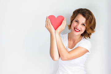 A young, happy woman holds a red heart in her hands, smiling broadly. Beautiful female, Girl on an isolated background in hands like. Valentines day and charity. Copy Space