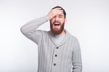 Face palm gesture is made by a young bearded man on white background.