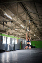 Female fitness model doing cross fit training on over head rings in a gym by pulling herself up