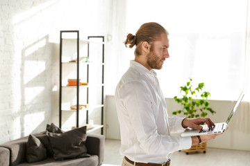 Photo of businessman wearing white shirt holding laptop in apartment