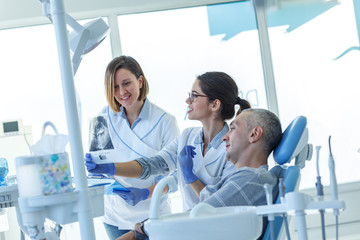 In a busy dental office, a group of dentists examining x-ray image of the patient's teeth to...