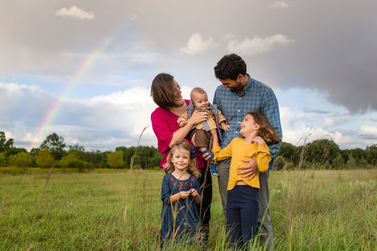 Portrait of young smiling family holding a baby outdoors with a rainbow in the background