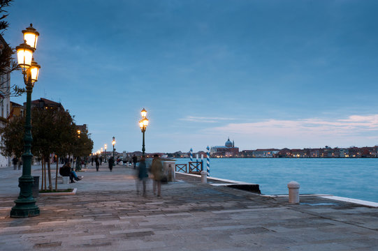 Tourists walk on the foundations of the Zattere in the Dorsoduro district of Venice. On the background the church of the Redentore or Redeemer on the Giudecca island, Italy.