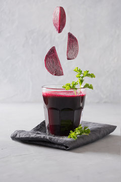 Glass of beetroot juice and flying sliced beet on grey. Close up. Vertical orientation.
