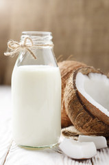 Glass bottle with milk or yogurt on white wooden kitchen table with coconut aside