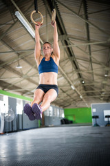 Fototapeta na wymiar Female fitness model doing cross fit training on over head rings in a gym by pulling herself up