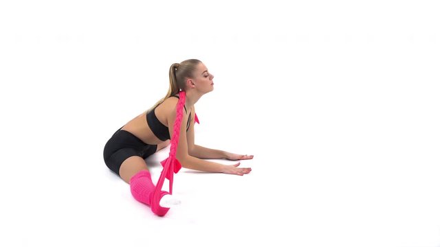 Side view of a young professional sportswoman doing stretching exercises using elastic rope (incline ahead in heel stretch position). Isolated, on white background