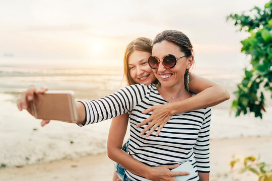 Two caucasian girlfriends hugging and posing for selfie on the Gulf of Thailand sea on Samui Island using smartphone. Careless vacation time concept image.
