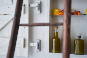detail closeup from a shelf in wall in country house rural style summer in spain.bottles oil vegetable paprika pepper lemon tomatos,blurred diffuse ladder in foreground