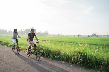 young couple wear helmets to ride folding bikes for sports in rice fields background