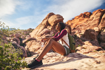 female hiker sitting on edge of cliff at red rock canyon with bottle of water