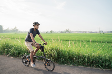Asian young male wear helmets to ride folding bikes in the rice fields in the morning