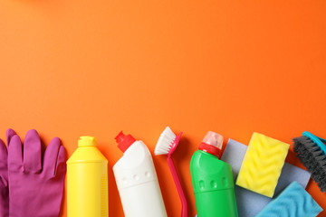 Bottles with detergent and cleaning supplies on orange background, space for text