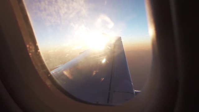 Sun flares hit the airplane window as the plane turns and the sun appears from behind the wing