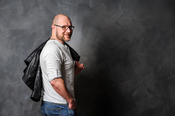 A man is standing against the wal. leather jacket thrown over