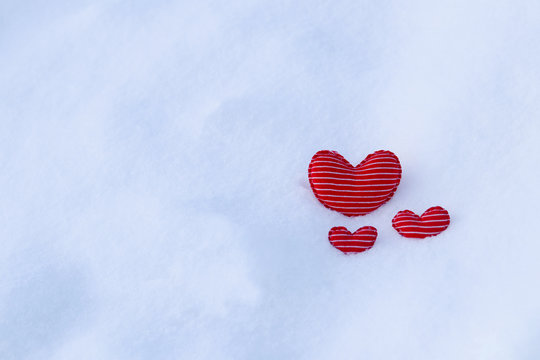 Three homemade textile soft hearts in red and white stripes on the cold snow in winter.  Selective focus. A gift for Valentine's day. Fabric hearts in the snow