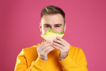 Young man eating tasty sandwich on pink background