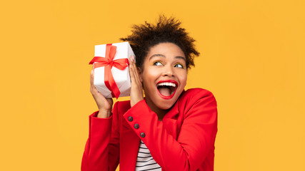 Happy black girl shaking gift box near ear - Powered by Adobe