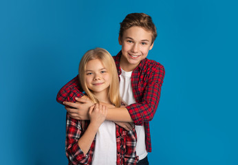 Happy siblings, brother and sister hugging and posing over blue background