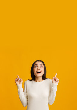 Excited millennial woman pointing upwards at copy space on yellow background