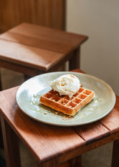 Home made classic waffle topping with a scoop of vanilla ice-cream. Topping with crush almond and maple syrup. Served in ceramic plate.