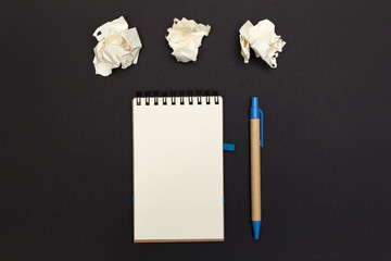 Crumpled paper balls with eco friendly pen and notebook with copy space on a black background....