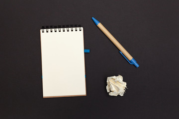 Notebook with copy space, eco friendly pen and crumpled paper ball on a black paper background. No ideas for message. Top view.
