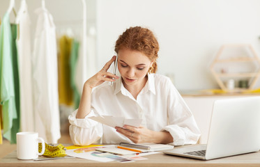 Young dressmaker talking by phone with customer, discussing order