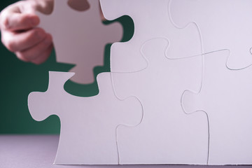 Hand holding piece of white puzzle on green background.