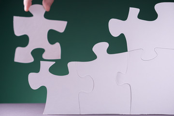 Hand holding piece of white puzzle on green background.
