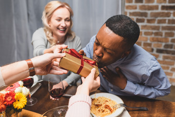 cropped view of man giving present to african american man during dinner