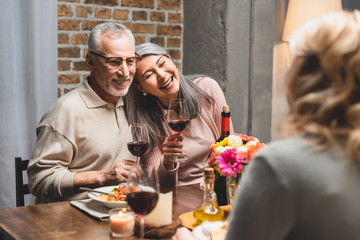 selective focus of smiling multicultural friends holding wine glasses during dinner