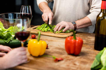 cropped view of woman holding wine glass and man cutting lettuce