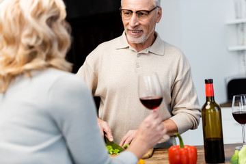 cropped view of woman talking with smiling friend and he cutting lettuce
